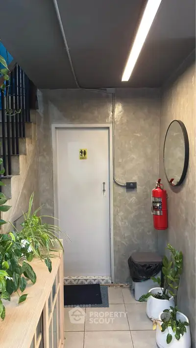Modern building entrance with plants and fire extinguisher, featuring a sleek design and ambient lighting.