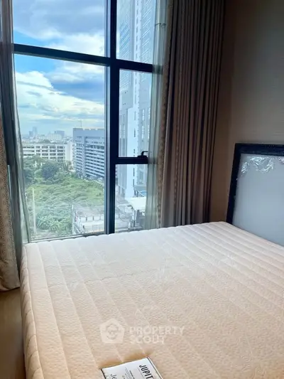 Spacious bedroom with large window offering stunning city views in modern high-rise apartment.