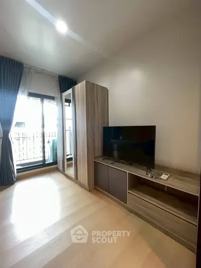 Modern living room with wooden flooring, TV unit, and balcony access in a stylish apartment.