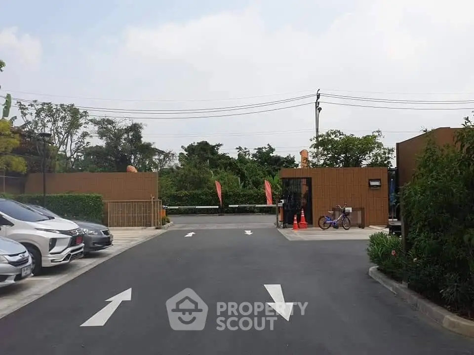 Modern gated entrance with ample parking and lush greenery, ideal for secure residential living.