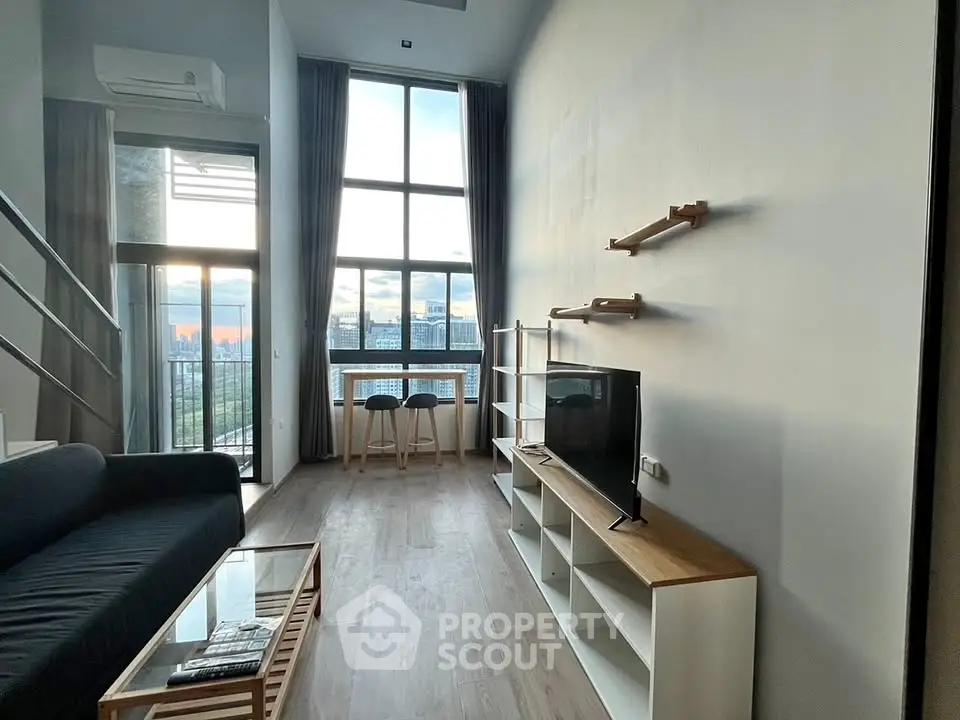Modern loft living room with high ceilings and large windows offering stunning city views.