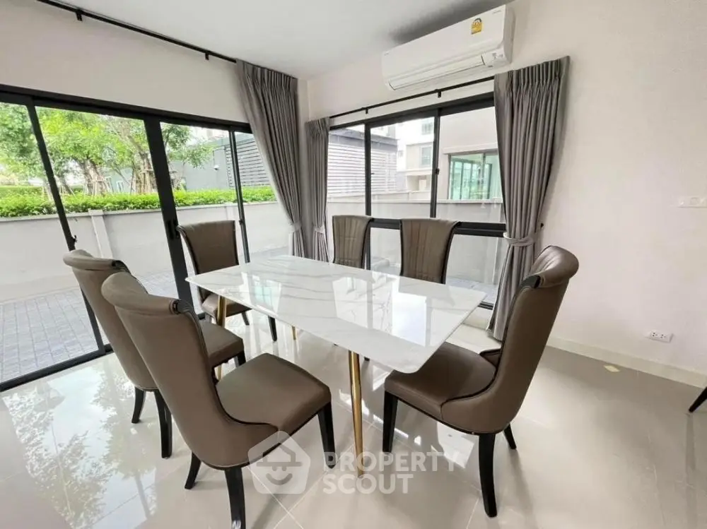 Elegant dining room with modern table and chairs, large windows, and lush outdoor view.