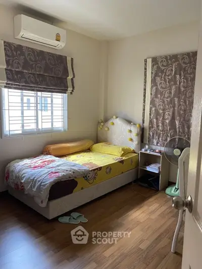 Cozy bedroom with wooden flooring and natural light, featuring a comfortable bed and air conditioning.