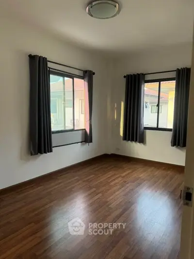 Spacious empty bedroom with wooden flooring and large windows in a modern home.