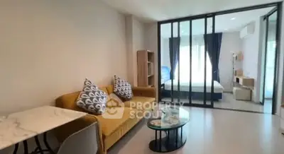 Modern living room with glass partition leading to bedroom, featuring stylish furniture.