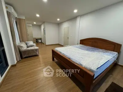 Spacious bedroom with wooden flooring and modern furniture in a well-lit apartment.