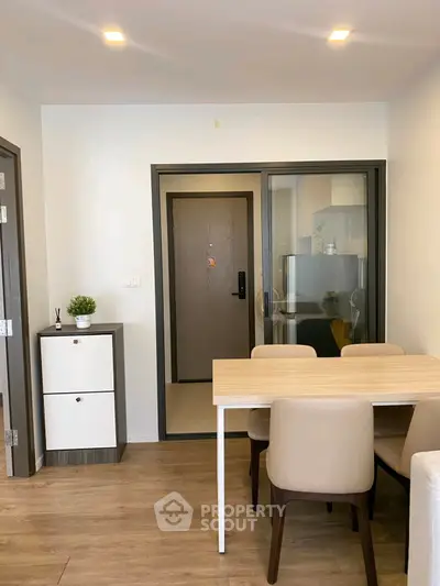 Modern dining area with wooden table and chairs, adjacent to a sleek glass door entrance.