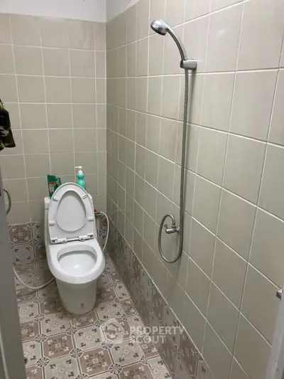 Compact bathroom with tiled walls and floor, featuring a toilet and shower setup.