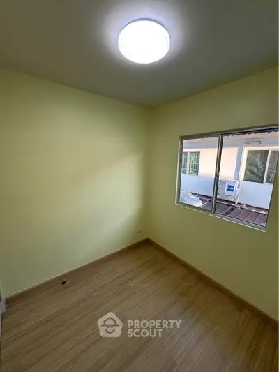 Bright empty room with wooden flooring and large window, perfect for customization.