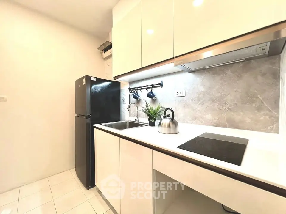 Modern kitchen with sleek white cabinets, black fridge, and electric cooktop in a compact layout.