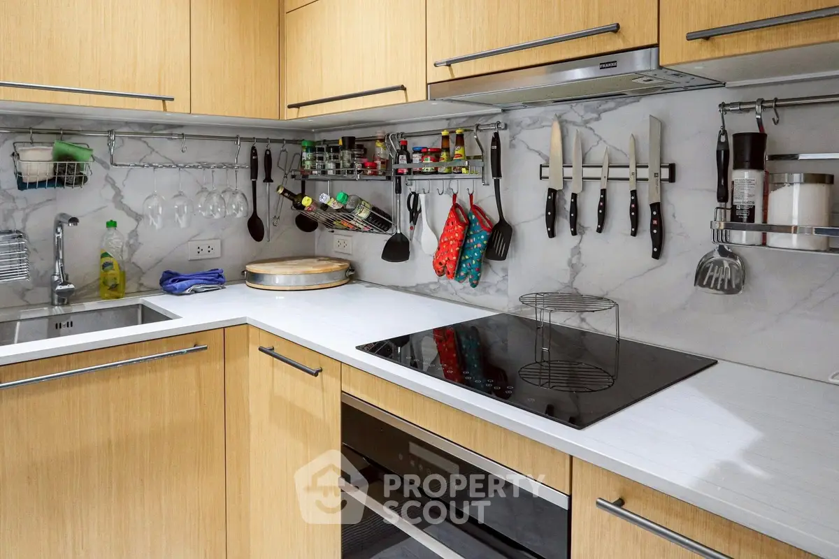 Modern kitchen with sleek cabinetry and built-in appliances, featuring a marble backsplash and organized utensils.