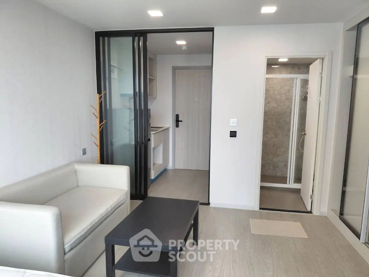 Modern living room with sleek design and glass partition leading to kitchen and bathroom.