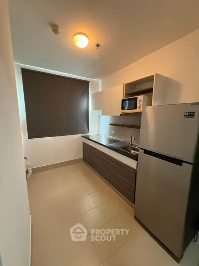 Modern kitchen with sleek cabinetry and stainless steel fridge in cozy apartment.