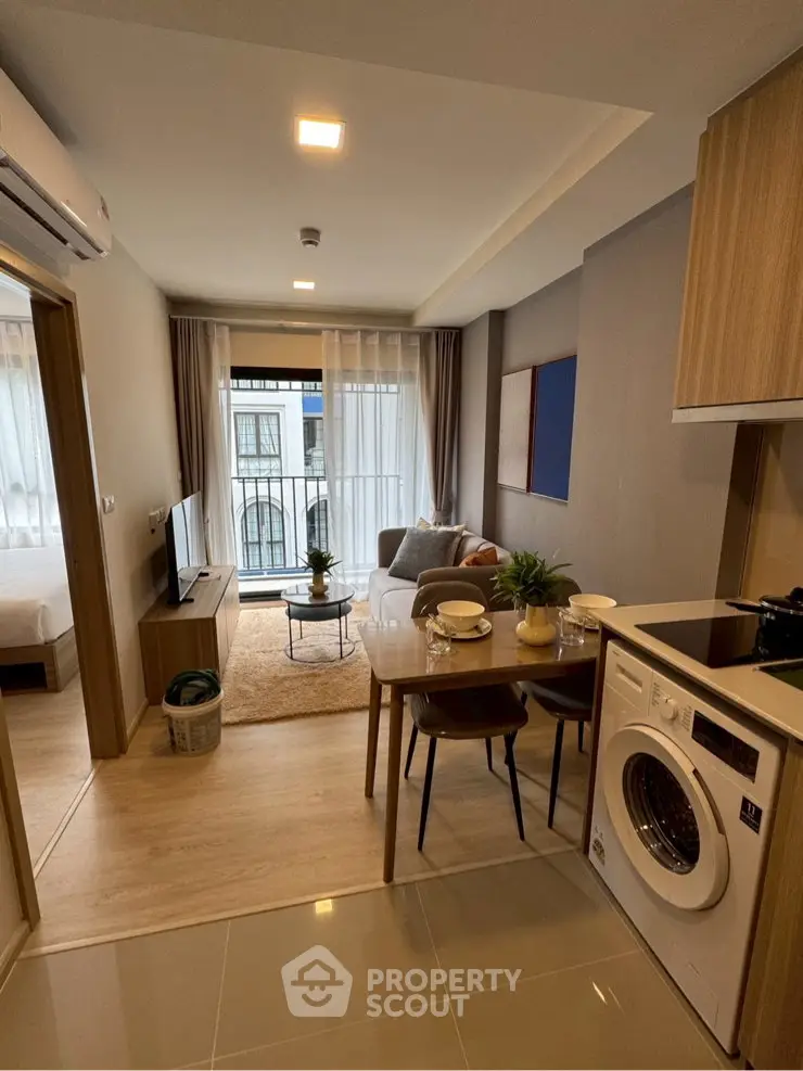 Modern apartment interior with open kitchen and cozy living room, featuring a washing machine and balcony view.