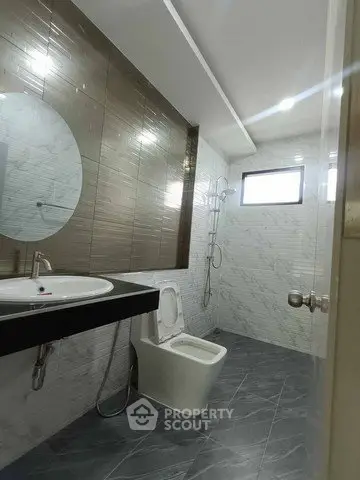 Modern bathroom with sleek design, featuring a round mirror, stylish tiles, and a spacious shower area.