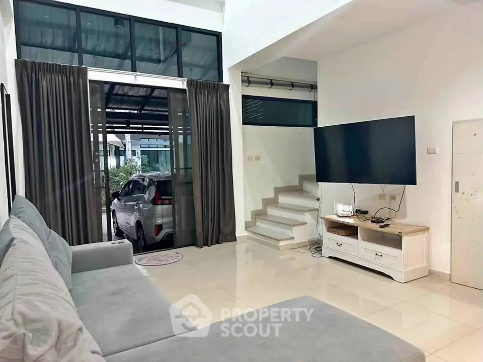 Spacious living room with modern decor and large TV, featuring a view of the carport through glass doors.