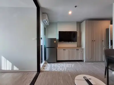 Modern living room with TV, fridge, and stylish cabinetry in a bright apartment.
