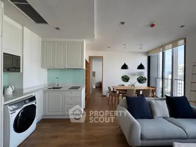 Modern open-plan living room and kitchen with city view, stylish furniture, and natural light.