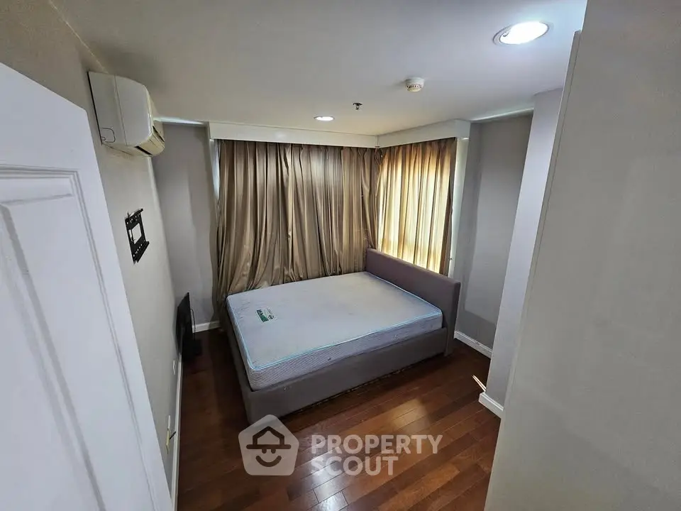 Cozy bedroom with wooden flooring and natural light, featuring a comfortable bed and air conditioning.