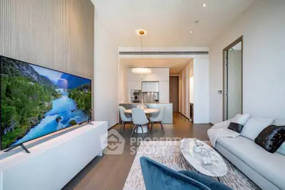 Modern open-plan living room with stylish decor and large TV, leading to a sleek kitchen area.