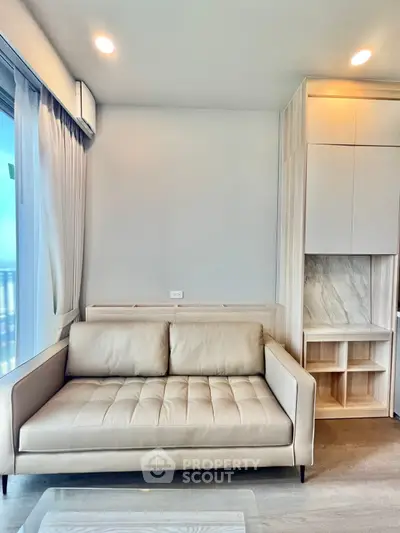 Modern living room with beige sofa and built-in storage, featuring large windows for natural light.