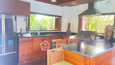 Luxurious kitchen with modern appliances and tropical garden view, featuring sleek wooden cabinetry and island seating.