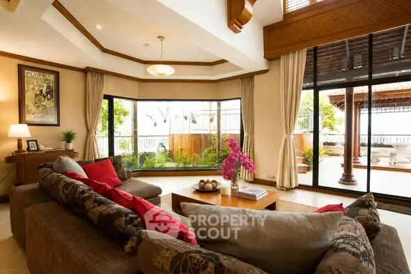 Luxurious living room with large windows and elegant decor, opening to a spacious balcony with garden views.