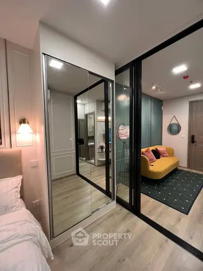 Modern bedroom with mirrored wardrobe and cozy living area in stylish apartment.