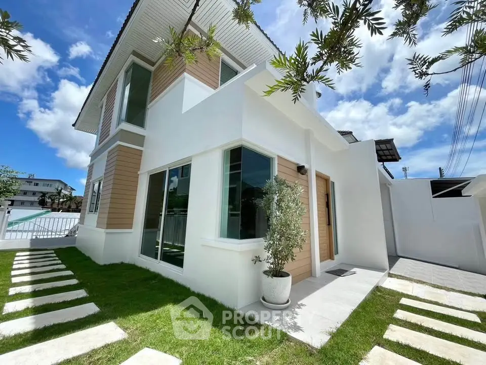 Modern two-story house with sleek design and lush green lawn under a bright blue sky.