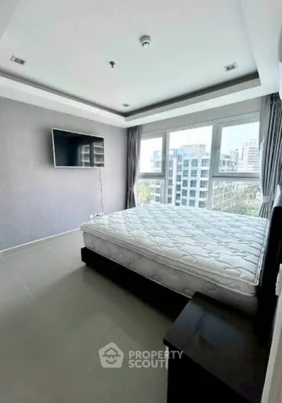 Modern bedroom with large windows and city view, featuring a wall-mounted TV and minimalist decor.