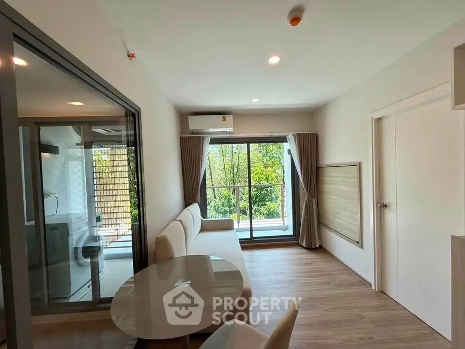 Modern living room with large window and garden view, featuring sleek furniture and natural light.