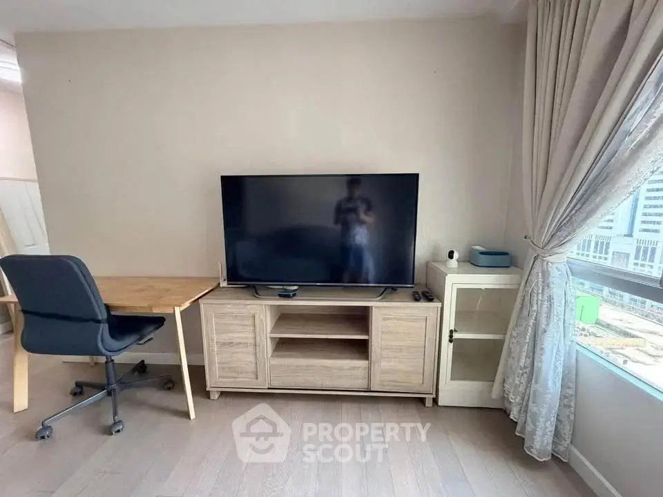Modern living room with TV, desk, and large window offering natural light.