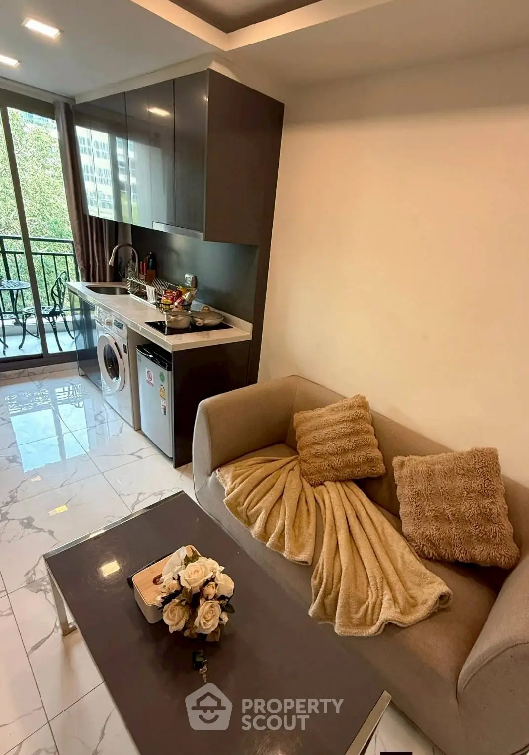 Modern living room with open kitchen and balcony view, featuring sleek furniture and appliances.