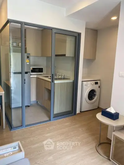 Modern compact kitchen with washing machine and glass partition in cozy apartment.