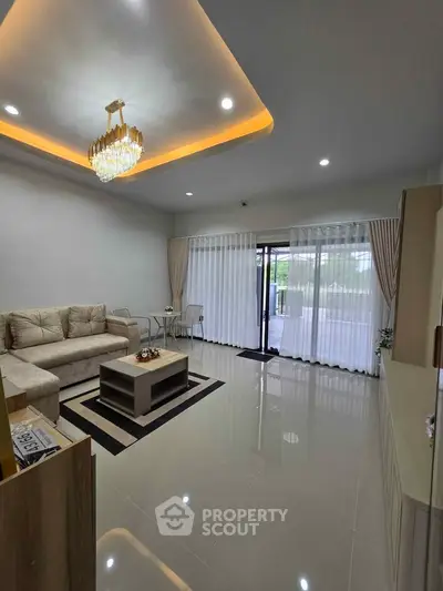 Spacious modern living room with elegant chandelier and large windows opening to a balcony.