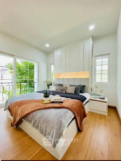 Modern bedroom with cozy decor and large windows offering natural light and garden view.