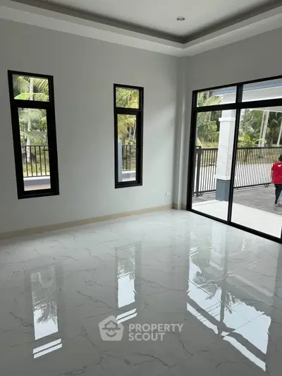 Spacious empty room with glossy marble floors and large windows overlooking a lush garden.