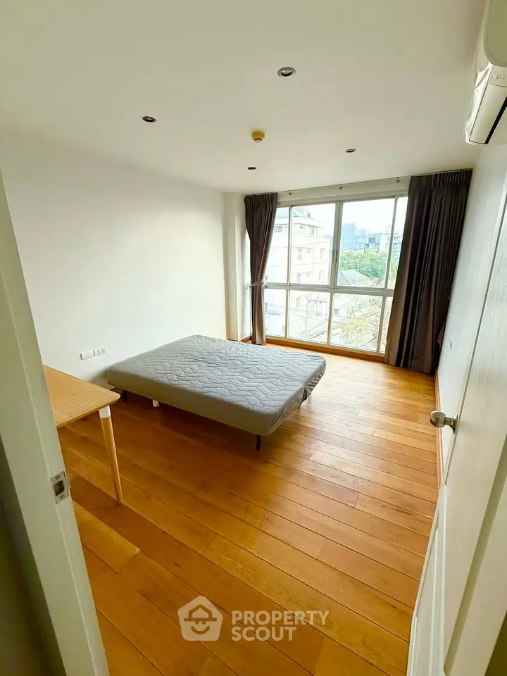 Spacious bedroom with large windows and wooden flooring offering a bright and airy atmosphere.