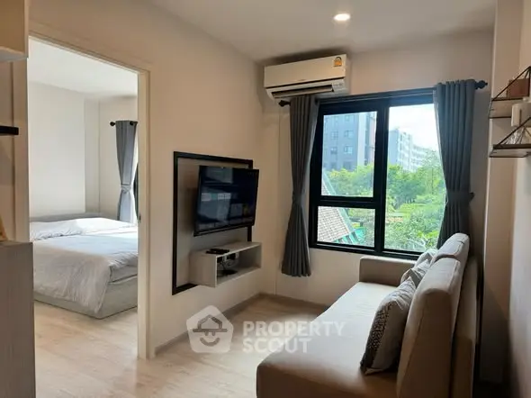 Modern apartment living room with cozy sofa and wall-mounted TV, adjacent to a bright bedroom with large window view.