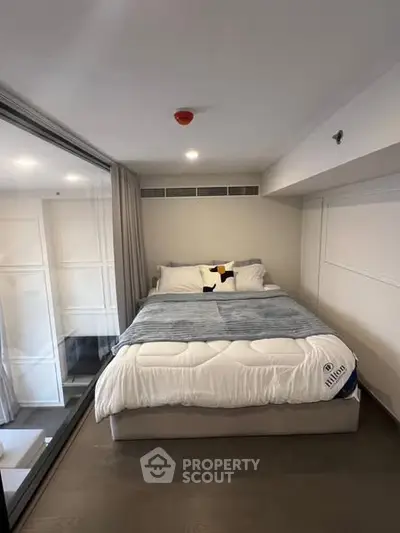 Cozy bedroom with modern decor and large window, perfect for relaxation.