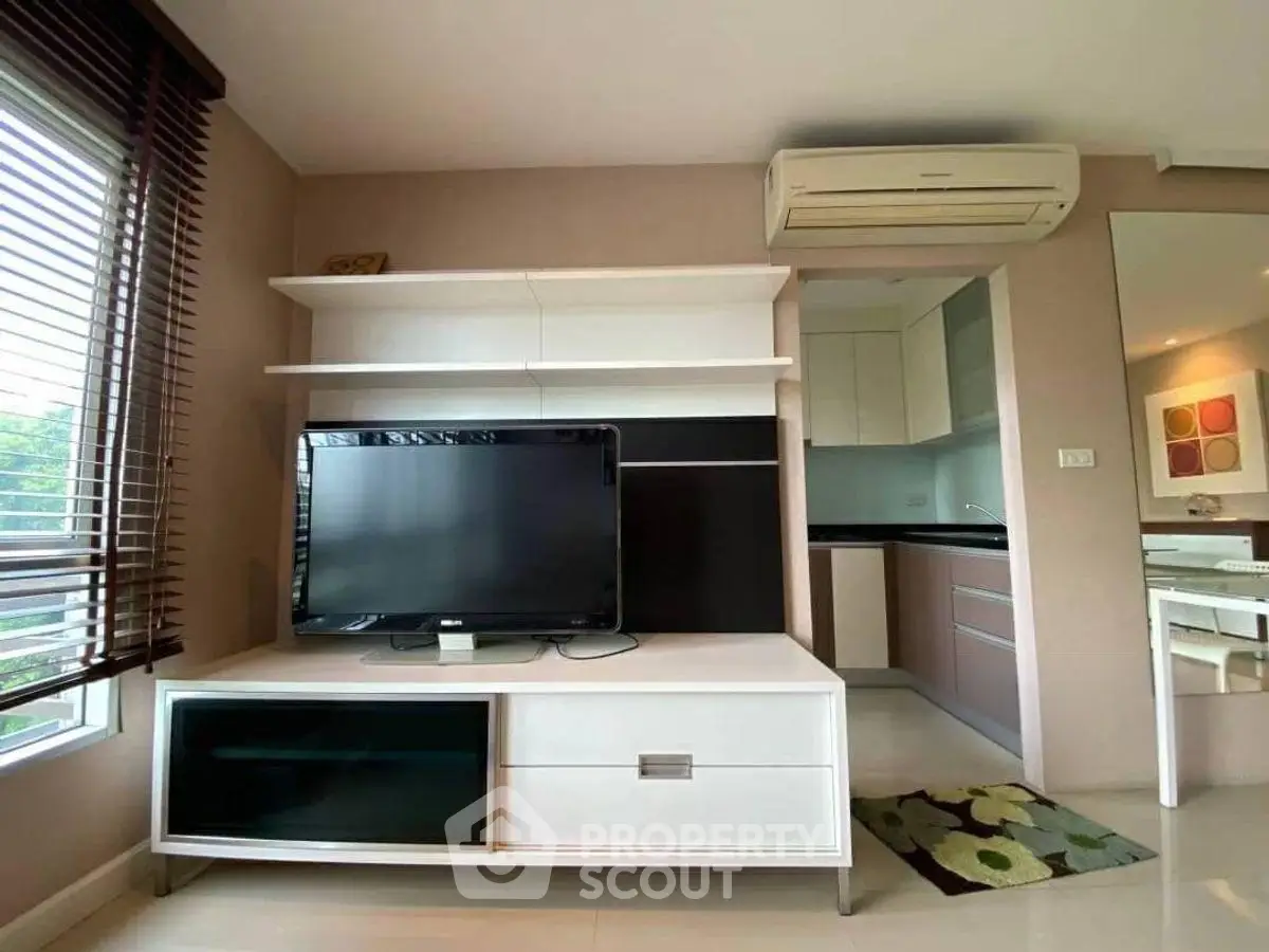 Modern living room with TV unit and air conditioning, adjacent to a sleek kitchen.