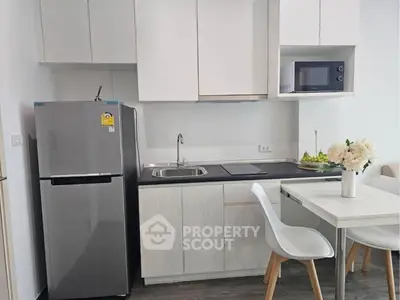 Modern kitchen with sleek appliances and minimalist design, featuring a fridge, microwave, and dining area.