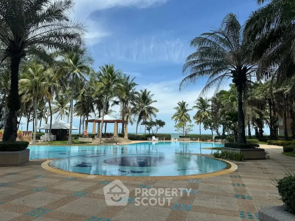 Luxurious beachfront pool area with palm trees and ocean view, perfect for relaxation.