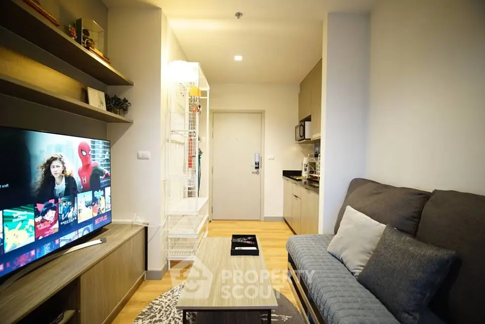 Modern living room with cozy sofa, wall-mounted TV, and compact kitchen area in a stylish apartment.