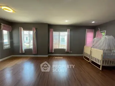 Spacious bedroom with wooden flooring and large windows, featuring a crib with a mosquito net.