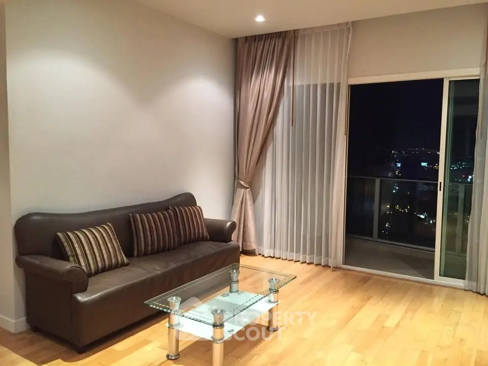 Modern living room with glass coffee table and city view balcony at night.