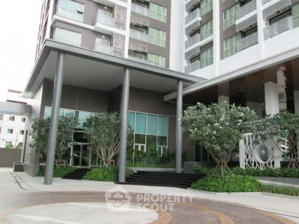 Modern apartment building entrance with landscaped greenery and sleek design.