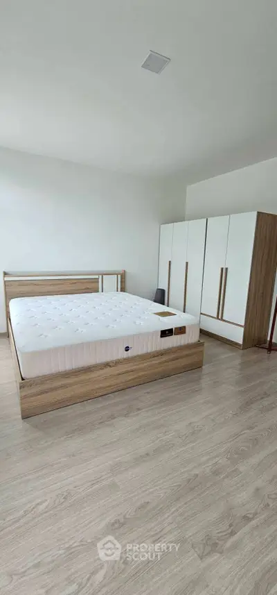 Spacious bedroom with modern wooden furniture and ample natural light.