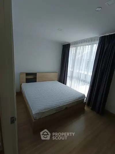 Cozy bedroom with wooden flooring and large window for natural light