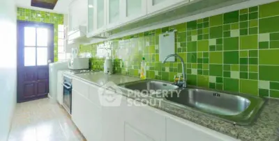 Bright kitchen with green tiled backsplash and modern appliances, featuring a double sink and ample counter space.